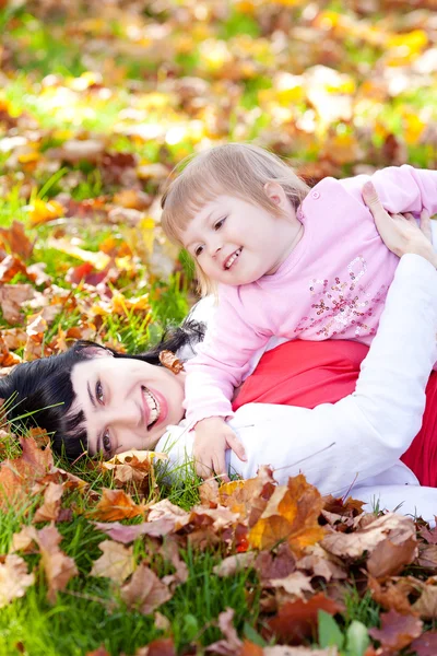 Mooie jonge moeder en haar dochter liggend op de herfst leav — Stockfoto