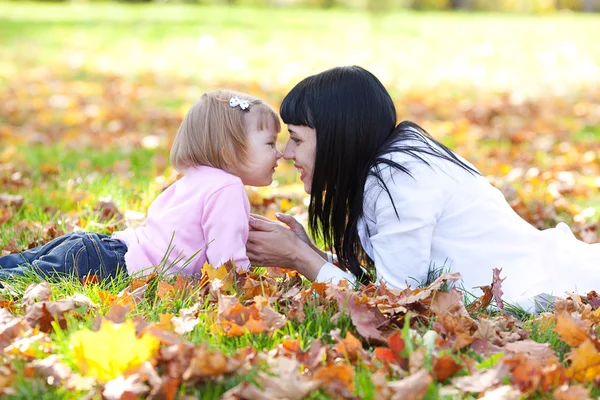 美丽的年轻母亲和她的女儿躺在秋天树叶上 — 图库照片