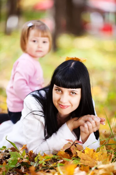 Beautiful young mother and her daughter lying on the autumn leav — Stock Photo, Image