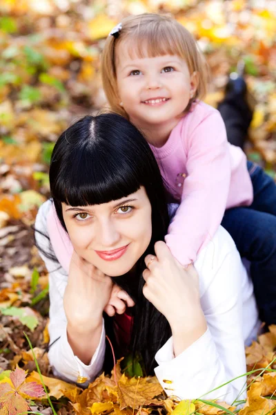 Beautiful young mother and her daughter lying on the autumn leav — Stock Photo, Image