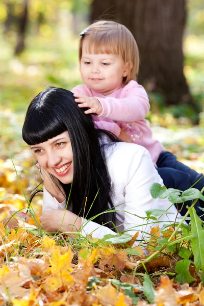 Beautiful young mother and her daughter lying on the autumn leav — Stock Photo, Image