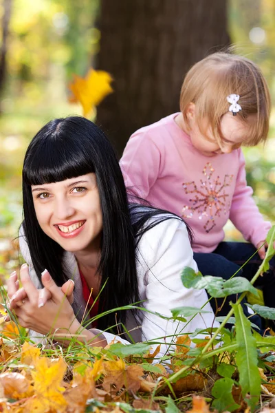 Schöne junge Mutter und ihre Tochter auf dem Herbstblatt liegend — Stockfoto