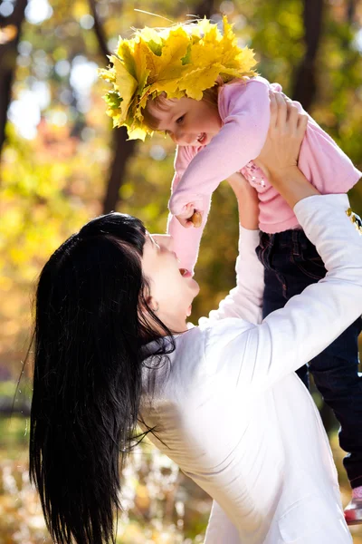 Mooie jonge moeder die haar dochter in een krans van esdoorn — Stockfoto