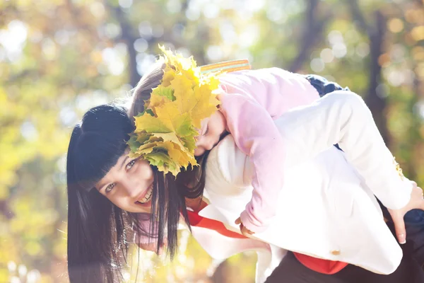Schöne junge Mutter hält ihre Tochter in einem Kranz aus Ahorn — Stockfoto