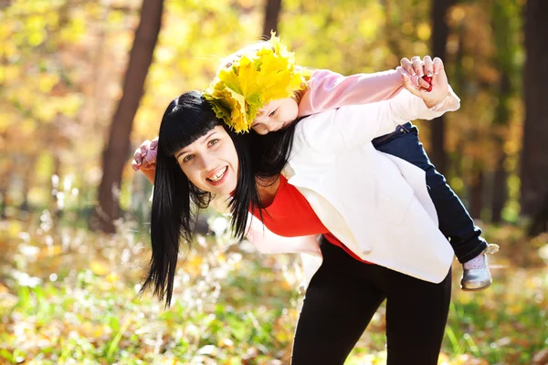 Schöne junge Mutter hält ihre Tochter in einem Kranz aus Ahorn — Stockfoto