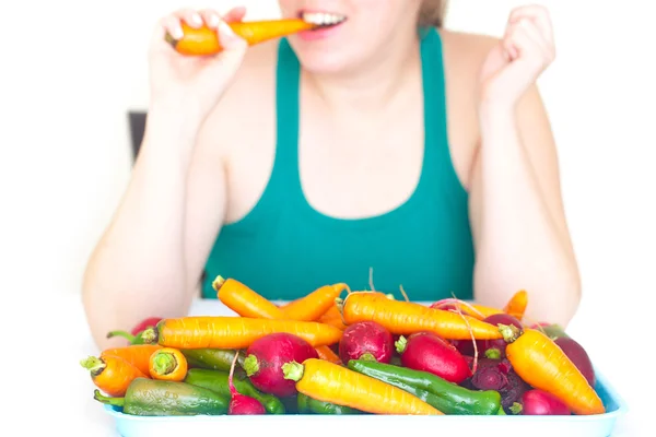 Young woman eating a carrot and a heap of vegetables — Stock Photo, Image