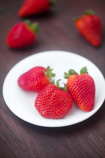 Röd saftiga jordgubbar i en tallrik på en trä yta — Stockfoto