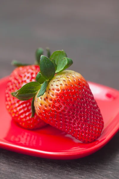 Rode sappige aardbei in rode plaat op een houten oppervlak — Stockfoto