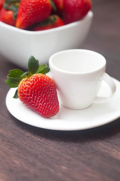 Rote saftige Erdbeere in einer Schüssel und Tasse auf einer Holzoberfläche Stockbild