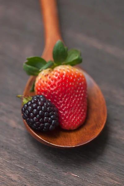 Kochlöffel mit Erdbeere und Brombeere auf einer Holzoberfläche Stockbild