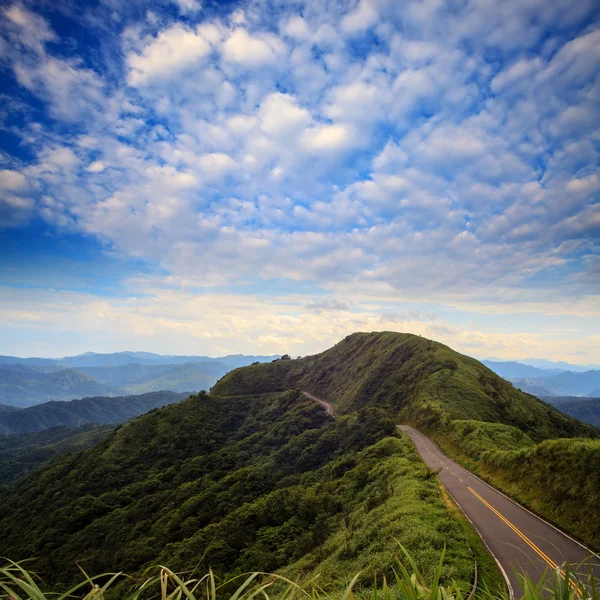 Route asphaltée à travers le champ vert et nuages sur ciel bleu — Photo