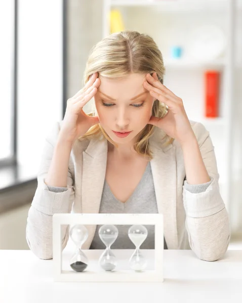 Mujer cansada detrás de la mesa con hourgalss — Foto de Stock