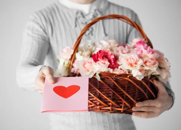 Homem segurando cesta cheia de flores e cartão postal — Fotografia de Stock