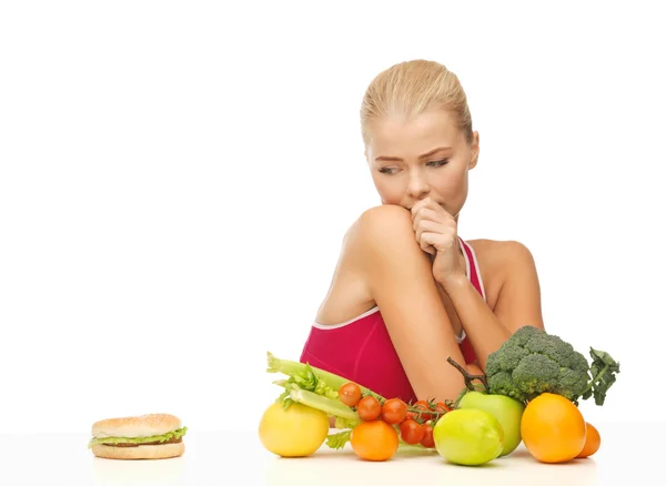 Doubting woman with fruits and hamburger — Stock Photo, Image