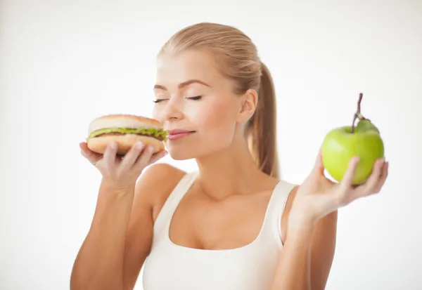 Mulher cheirando hambúrguer e segurando maçã — Fotografia de Stock