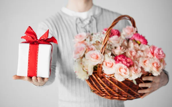 Homem segurando cesta cheia de flores e caixa de presente — Fotografia de Stock