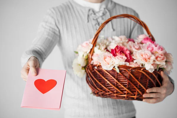 Homem segurando cesta cheia de flores e cartão postal — Fotografia de Stock