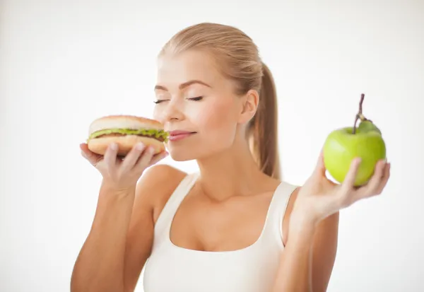 Frau riecht Hamburger und hält Apfel in der Hand Stockfoto