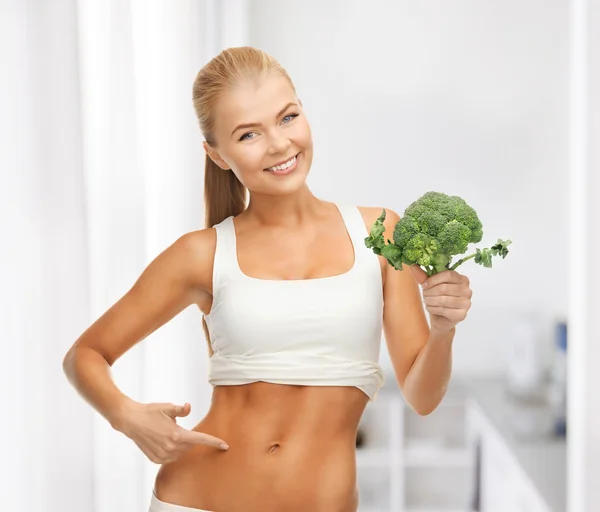 Vrouw wijzend op haar abs en houden van broccoli — Stockfoto