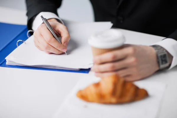 何かを書くコーヒーを持ったビジネスマン — ストック写真