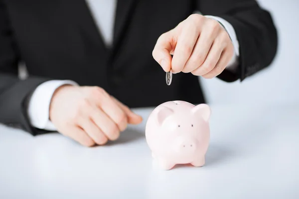 Man putting coin into small piggy bank — Stock Photo, Image