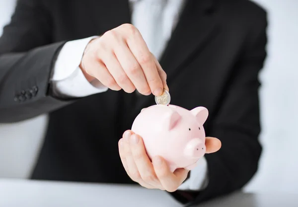 Man putting coin into small piggy bank — Stock Photo, Image