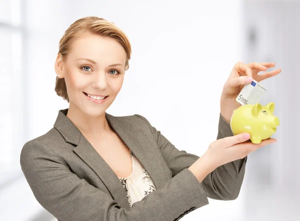 Woman putting cash money into small piggy bank — Stock Photo, Image