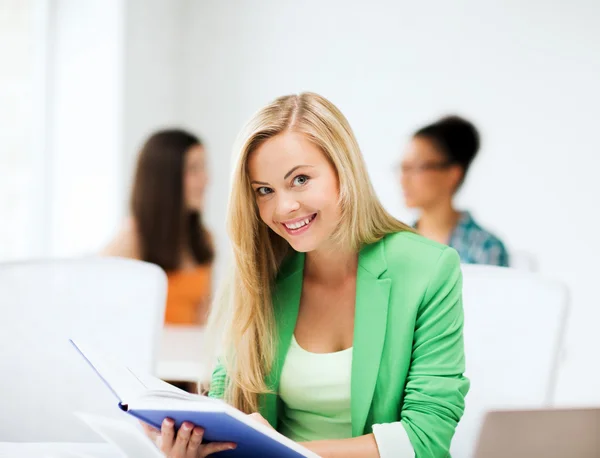 Chica sonriente estudiante leyendo libro en la escuela — Foto de Stock