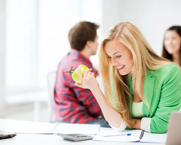 Lächelnde Schülerin isst in der Schule Apfel Stockfoto