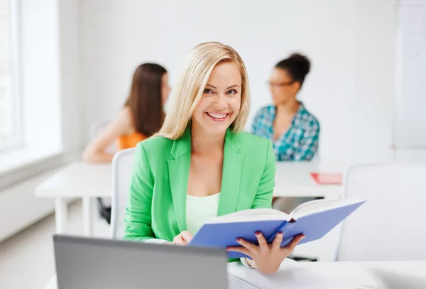 Smiling young girl reading book at school — Stock Photo, Image