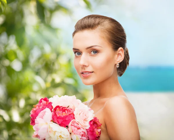 Vrouw oorbellen dragen en houden van bloemen — Stockfoto