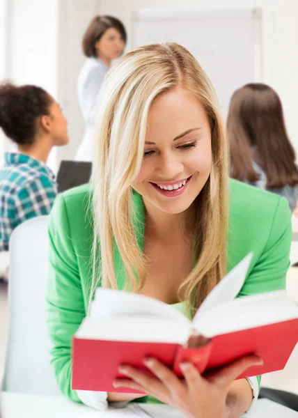 Estudante sorrindo livro de leitura menina na escola — Fotografia de Stock