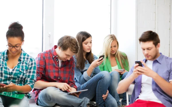 Estudiantes mirando dispositivos en la escuela — Foto de Stock