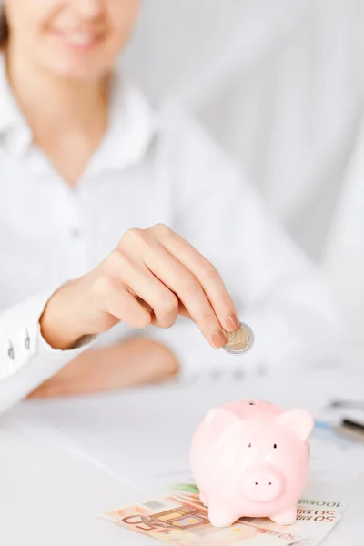 Mulher mão colocando moeda em pequeno banco porquinho — Fotografia de Stock
