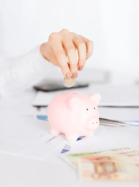 Woman hand putting coin into small piggy bank — Stock Photo, Image