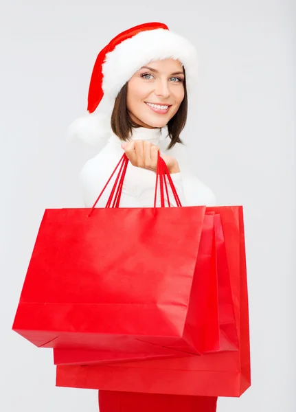 Vrouw in helper kerstmuts met shopping tassen — Stockfoto