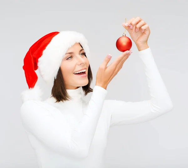 Kobieta w santa hat pomocnika z Boże Narodzenie ball — Zdjęcie stockowe
