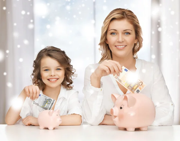 Mãe e filha com bancos porquinhos e dinheiro Fotografia De Stock