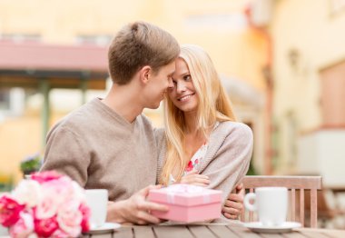 Romantic happy couple with gift in the cafe clipart