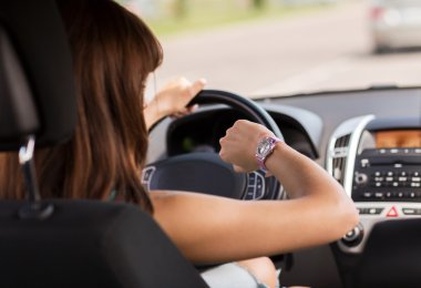 Woman driving a car and looking at watch clipart