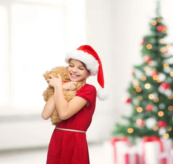 Oyuncak ayı ile santa yardımcı şapkalı kız gülümseyerek — Stok fotoğraf