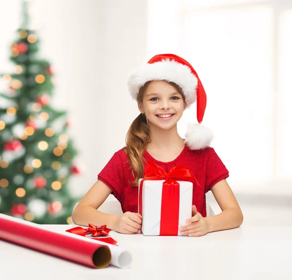 Chica sonriente en sombrero de ayudante de santa con caja de regalo — Foto de Stock