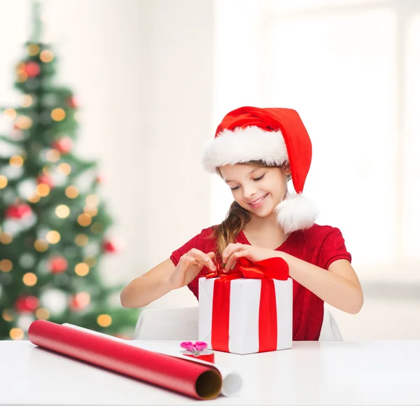 Chica sonriente en sombrero de ayudante de santa con caja de regalo — Foto de Stock