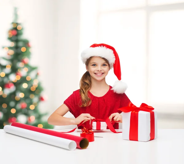 Chica sonriente en sombrero de ayudante de santa con caja de regalo — Foto de Stock