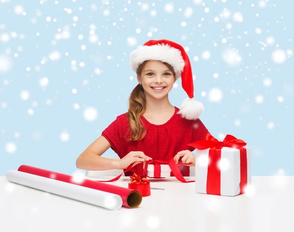 Chica sonriente en sombrero de ayudante de santa con caja de regalo — Foto de Stock