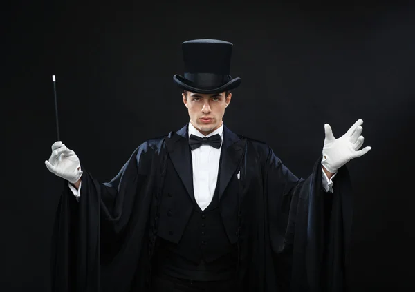 Magician in top hat with magic wand showing trick — Stock Photo, Image