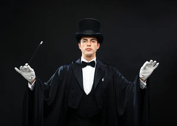 Magician in top hat with magic wand showing trick — Stock Photo, Image