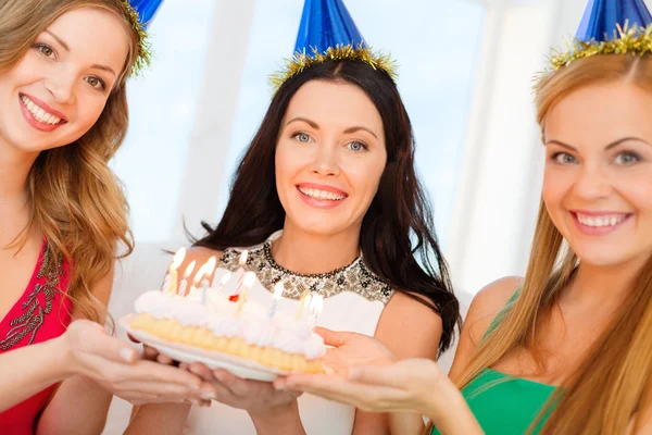 Three women wearing hats holding cake with candles — Stock Photo, Image