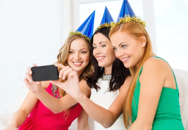 Tre donne sorridenti in cappelli divertirsi con la macchina fotografica — Foto Stock