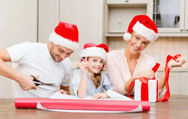 Smiling family in santa helper hats with gift box — Stock Photo, Image